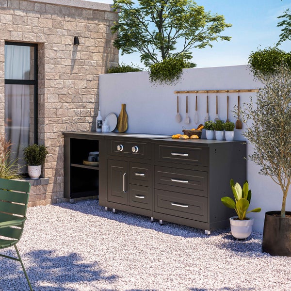 Moderne, organisierte Außenküche in Anthrazit mit Modulschränken und Schubladen auf einer hellen Kiesfläche vor einer Steinwand im Garten.
