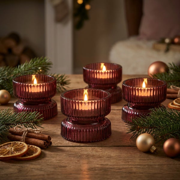 Vier brennende Stumpenkerzen in geriffelten Glaswindlichtern als festliche Tischdekoration mit Tannenzweigen und Weihnachtsdeko.