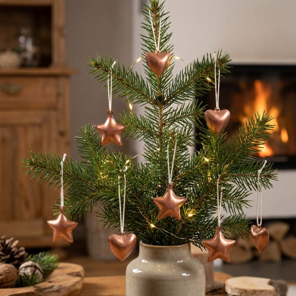 Weihnachtsbaumschmuck aus Metall in Stern- und Herzform zum Aufhängen an einer Tanne in einer Vase vor einem Kamin.