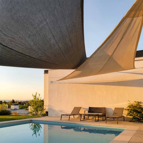 Zwei Sonnensegel in Grau und Beige über einer Terrasse mit Pool, Sonnenliegen und Gartenmöbeln vor einer Hauswand.