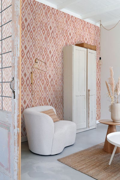 Wohnzimmer mit gemusterter Tapete, Sessel und Schrank