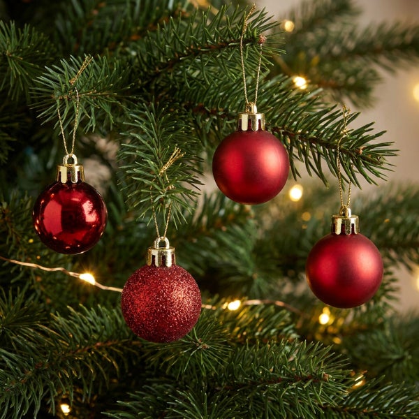 Vier verschiedene rote Weihnachtsbaumkugeln hängend an den Zweigen eines Tannenbaums mit Lichterkette