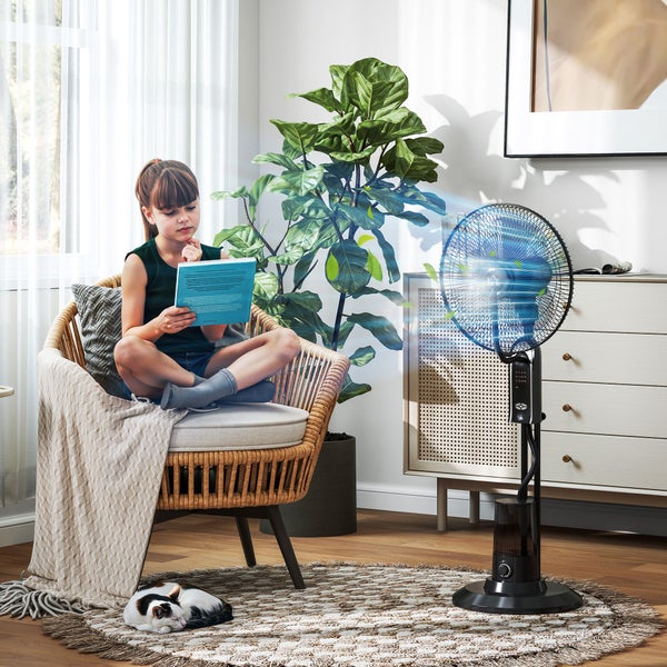 Schwarzer Standventilator mit Sprühnebelfunktion in hellem Wohnzimmer mit lesendem Kind, Zimmerpflanze und Kommode.