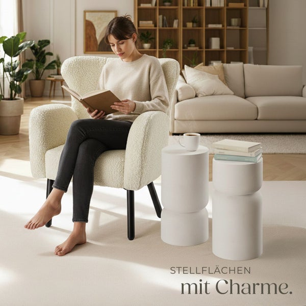 Helle Wohnzene mit Frau lesend in einem Sessel, Beistelltischen und Sofa