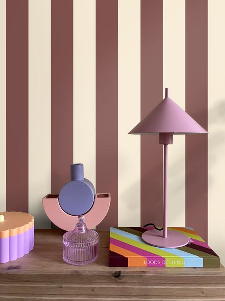 Hell gestaltete Szene mit gestreifter Tapete an der Wand, einer hölzernen Ablage, einer Tischlampe und dekorativen Vasen.