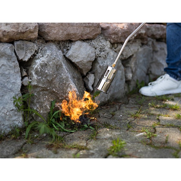 Unkrautbrenner aus Metall vernichtet Unkraut an einer Steinmauer mit einer offenen Flamme.