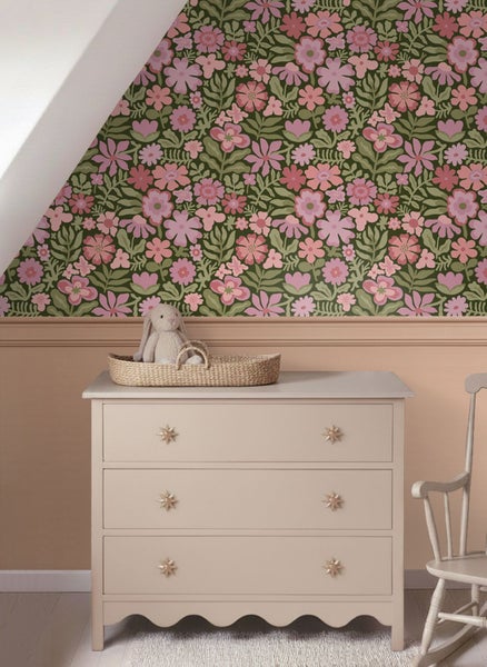 Kinderzimmer mit floraler Tapete, rosa Blumen auf Grün. Helle Kommode mit Sterngriffen und ein Stoffhase in einem Korb.