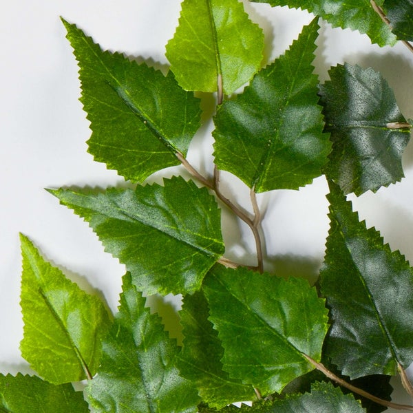 Künstlicher Baum mit grünen Blättern und braunem Stamm in einem schwarzen Kunststofftopf.