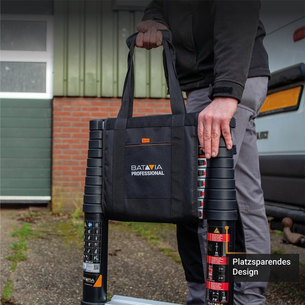 Eine Person trägt eine zusammengeschobene Batavia Professional Teleskopleiter in einer Tragetasche, platzsparendes Design.