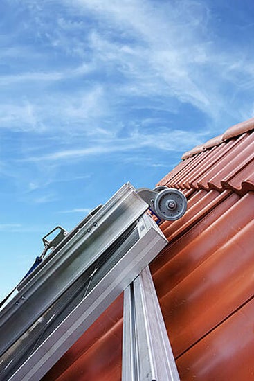 Dachdeckerleiter mit Rolle auf einem Ziegeldach vor blauem Himmel