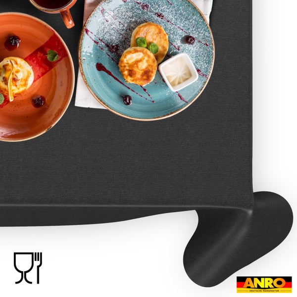 Schwarze Tischdecke in Textiloptik mit hellem, organisiertem Frühstücksgedeck auf Tellern. Symbol für Lebensmittelechtheit und ANRO Logo.