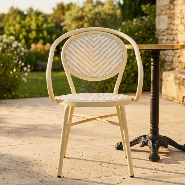 Bistrostuhl aus Metall mit geflochtener Sitzfläche und Rückenlehne im Chevron-Muster, helle Außenansicht auf einer Terrasse neben einem Tisch.