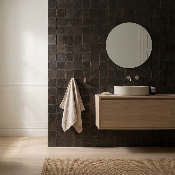Modernes Badezimmer mit Waschtisch, rundem Spiegel und Wandfliesen in quadratischer Optik vor einer dunklen Akzentwand.