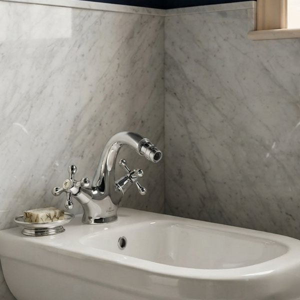 Klassische Zwei-Griff-Bidetarmatur aus Chrom mit Kreuzgriffen, montiert auf einem weißen Keramik-Bidet vor einer Wand in Marmoroptik.