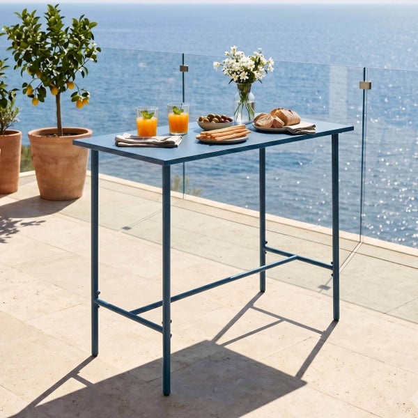Hoher rechteckiger Gartentisch aus Metall auf einer hellen Terrasse mit Meerblick, gedeckt mit Getränken, Snacks und einer Blumenvase.