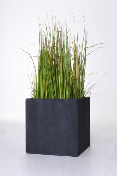 Künstliches Gras in einem quadratischen schwarzen Pflanzgefäß mit strukturierter Oberfläche.