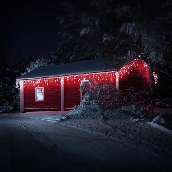 Ein rotes Gartenhaus im Schnee bei Nacht, festlich geschmückt mit einer leuchtenden LED Lichterkette unter dem Dach.
