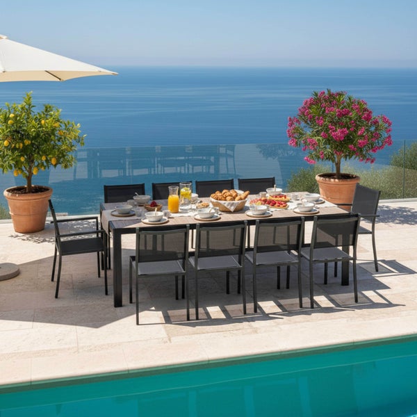 Große Garten-Essgruppe auf einer hellen Steinterrasse mit Meerblick und Pool. Dunkle Metallstühle stehen an einem gedeckten Tisch.