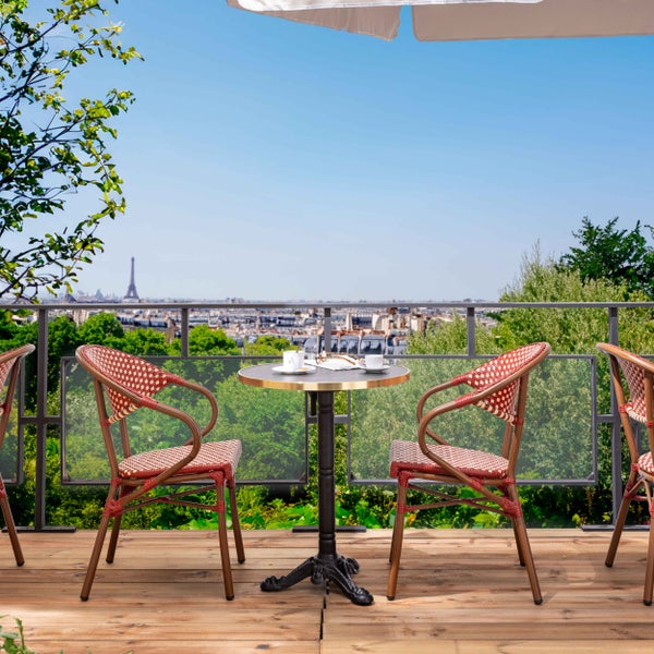 Bistro-Set mit zwei geflochtenen Stühlen und rundem Tisch auf einer Holzterrasse mit Blick auf Paris.