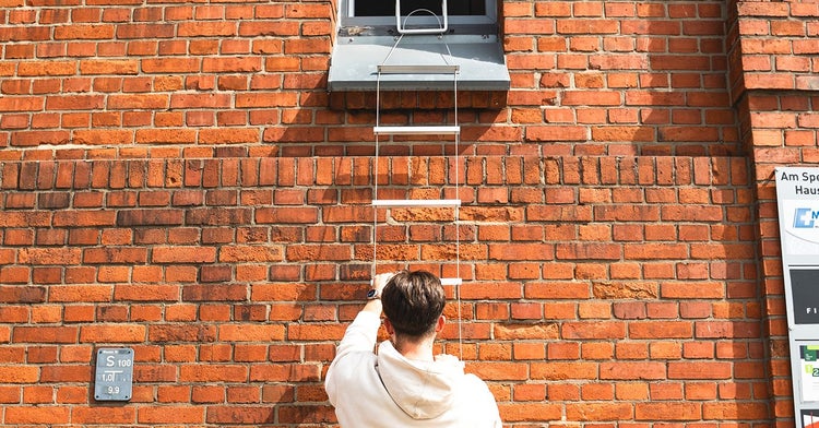 Mann klettert auf einer Notleiter an einer Ziegelmauer