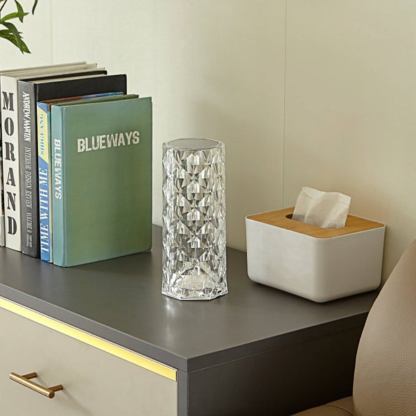 Zylindrische Dekorationsleuchte mit Kristalleffekt auf einem Schreibtisch neben Büchern und einer Taschentuchbox.