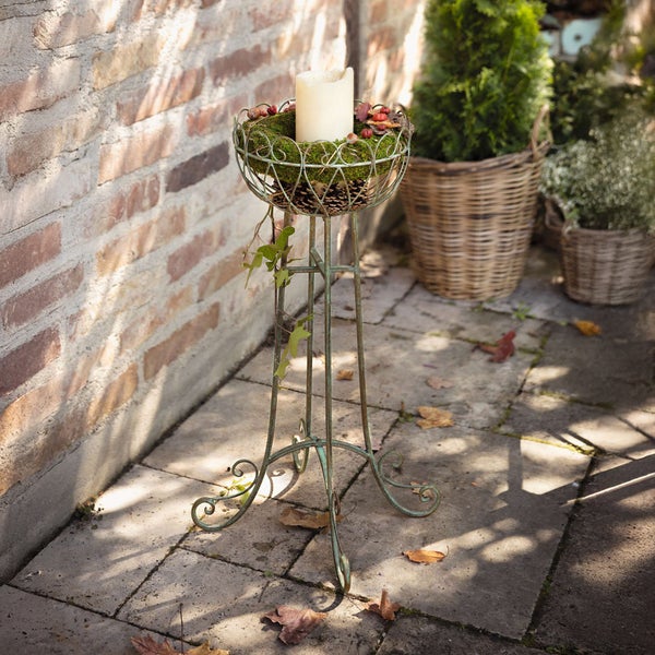 Dekorative Pflanzensäule aus Metall mit Kerze und herbstlicher Dekoration im Außenbereich.