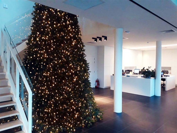 Großer beleuchteter Weihnachtsbaum in einem modernen, offenen Bürogebäude mit Treppe und Empfangstheke.