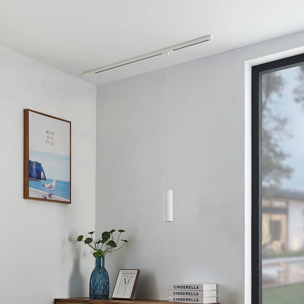 Weiße, zylindrische Pendelleuchte für ein Schienensystem in einem hellen, modern eingerichteten Zimmer mit Sideboard und Wandbild.