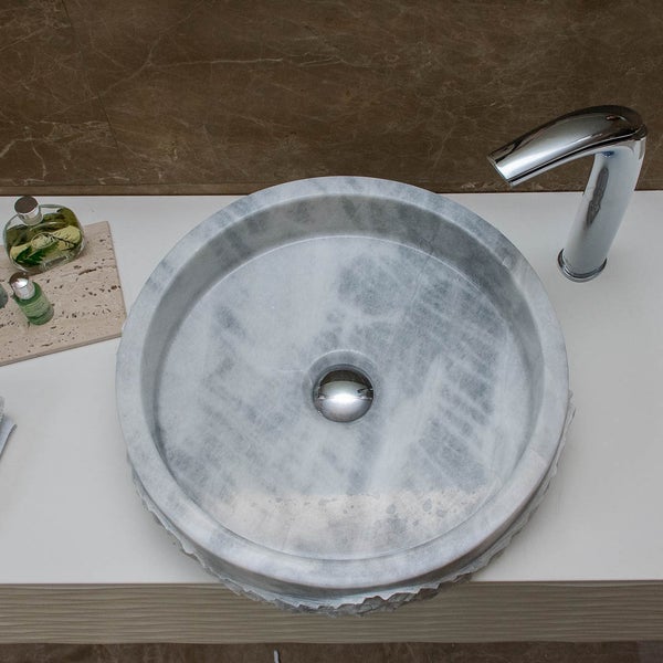 Rundes Aufsatzwaschbecken aus Marmor mit verchromter Armatur auf einer Waschtischplatte.