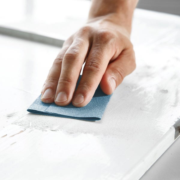 Eine Hand schleift eine Oberfläche mit Schleifpapier.