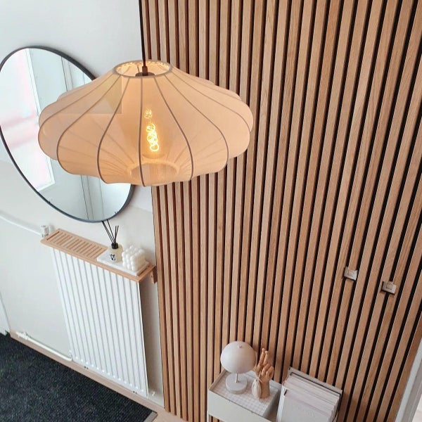 Modernes Interieur mit einer Wandverkleidung aus Holzlamellen, einer dekorativen Pendelleuchte aus Stoff und einem runden Spiegel.
