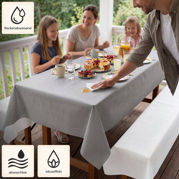 Eine Familie isst auf der Terrasse, während ein Mann eine verschüttete Flüssigkeit von einer fleckenabweisenden und abwaschbaren Tischdecke wischt.