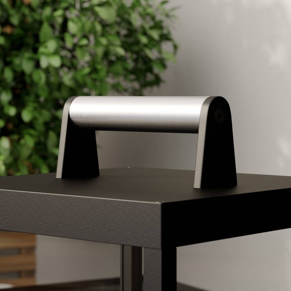 Nahaufnahme eines silbernen Griffs aus gebürstetem Metall an einem schwarzen Gehäuse vor einem Hintergrund mit Pflanzen.