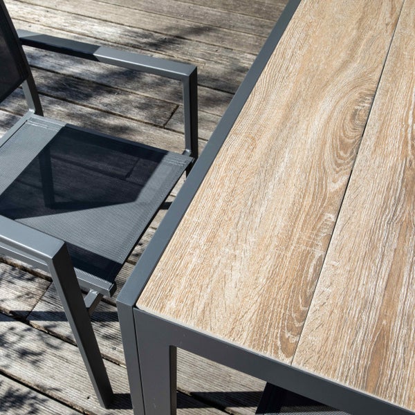 Gartentisch mit Tischplatte in Holzoptik und Metallgestell neben passendem Gartenstuhl mit Netzbespannung auf einer Holzterrasse.