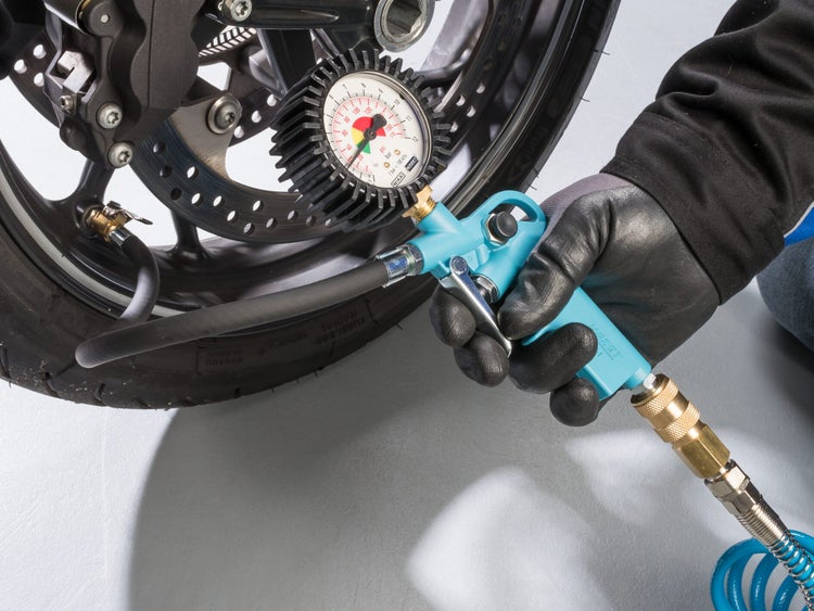 Person prüft mit einem Hazet Reifenfüllmessgerät den Luftdruck an einem Motorradreifen in einer Werkstatt.