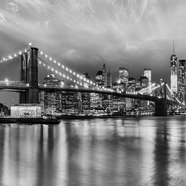 Schwarzweißaufnahme der Brooklyn Bridge und der Skyline von New York bei Nacht.