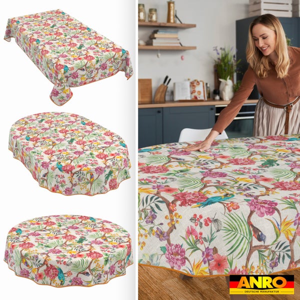 Abwaschbare Wachstischdecke mit tropischem Muster aus Papageien und Blumen in verschiedenen Formen. Frau in der Küche. ANRO Logo.
