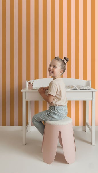 Mädchen sitzt an einem Schreibtisch vor einer gestreiften Tapete