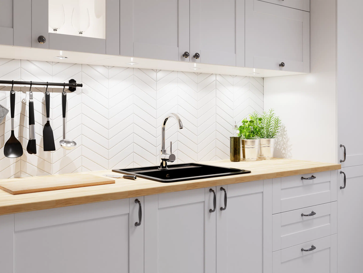 Moderne helle Küche mit grauen Schränken, Holz-Arbeitsplatte, schwarzer Spüle, Chrom-Armatur und weißem Fliesenspiegel im Fischgrätmuster.