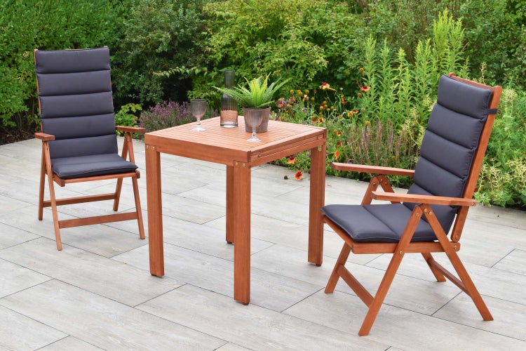 Gartenszene mit Holztisch, zwei Stühlen mit Auflagen, Gläsern und Dekoration im Freien.