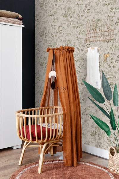 Einrichtung eines Kinderzimmers mit einem Babybett aus Rattan, einem Baldachin, einer Zimmerpflanze und einer Tapete mit Pflanzenmotiven.