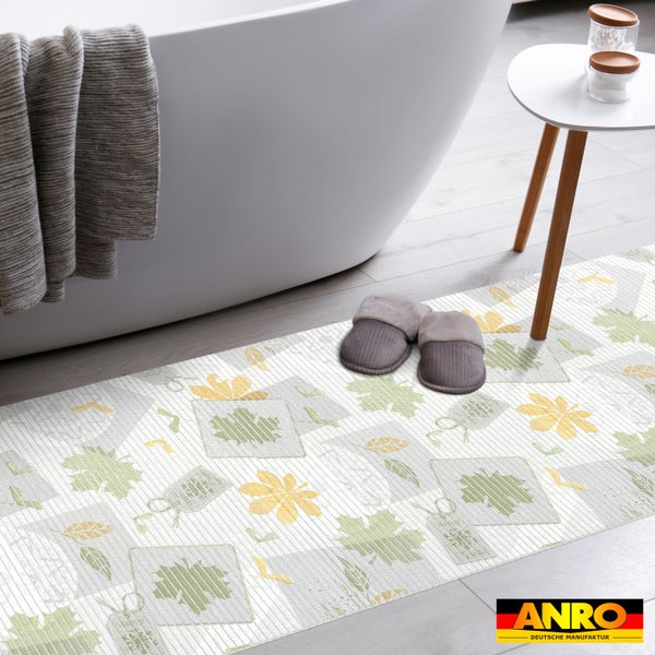 Badezimmer-Läufer mit Blattmuster vor weißer Badewanne, graue Hausschuhe und Beistelltisch, ANRO Deutsche Manufaktur Logo.
