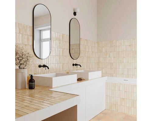 Modernes, helles Badezimmer mit zwei weißen Aufsatzwaschbecken, ovalen Spiegeln mit schwarzem Rahmen und vertikalen beigen Wandfliesen.
