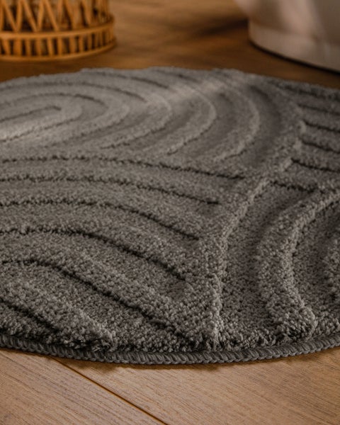 Runder grauer Badeteppich mit Wellenstruktur auf Holzfußboden.