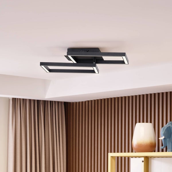 Moderne schwarze LED-Deckenleuchte aus zwei versetzten Rechtecken in einem hellen Raum mit Holzlamellenwand und Vorhängen.