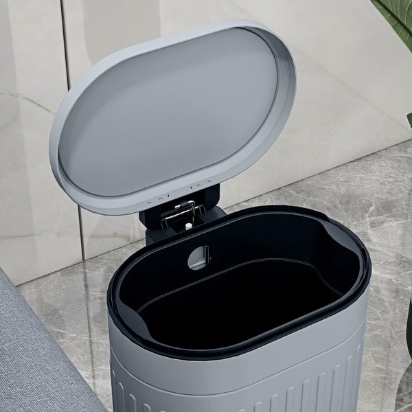 Offener grauer Mülleimer in ovaler Form mit schwarzem Inneneimer in einem modern eingerichteten Raum.