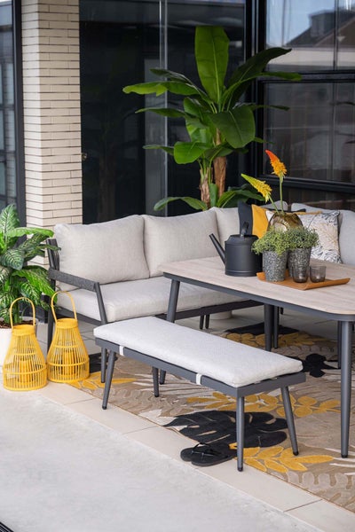 Moderne Garten-Lounge-Gruppe auf einer Terrasse mit grauem Ecksofa, Sitzbank, hellem Polster, Holzeffekt-Tisch, Outdoor-Teppich und gelber Deko.