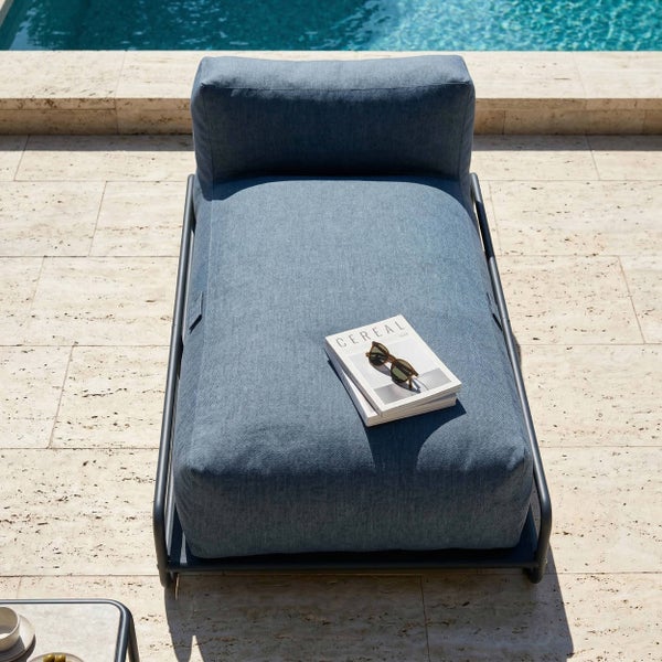 Moderne Sonnenliege mit blauem Polster auf einer Terrasse am Pool, minimalistisches Design mit dunklem Metallrahmen.