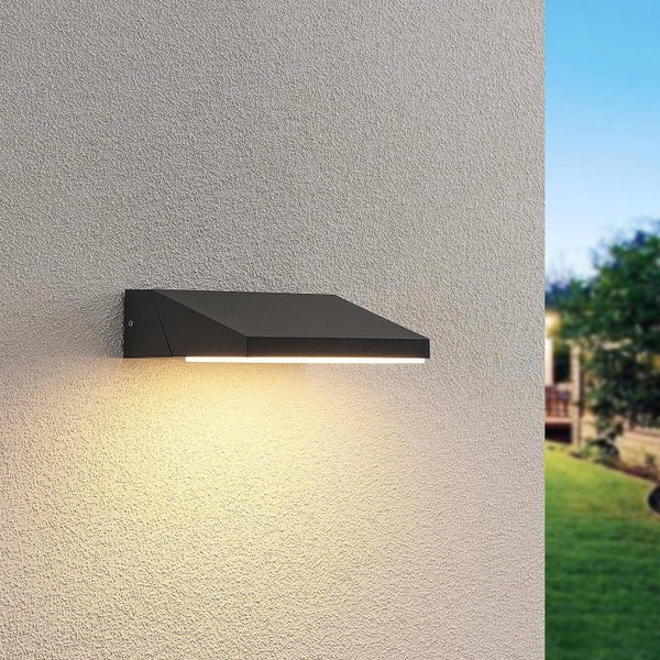 Moderne, keilförmige Außenwandleuchte in Schwarz an einer strukturierten Fassade mit Lichtaustritt nach unten.