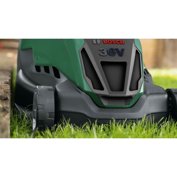 Bosch 36 Volt Rasenmäher mäht Gras an einer Steinkante. Bosch Logo und 36 Volt Schriftzug auf dem Gehäuse.